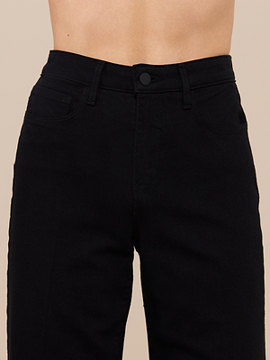 A close-up of a person wearing the Scottie Wide-Leg Jean in high-rise black premium stretch denim, highlighting the waistband, front pockets, and button closure against a neutral background. The face is not shown.