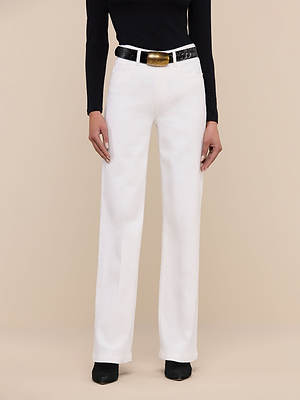 A person in a black long-sleeve top, Scottie Wide-Leg Jean in white with a high-rise waistband, a black textured belt featuring a gold buckle, and black shoes stands against a beige background. The image is cropped at the shoulders.
