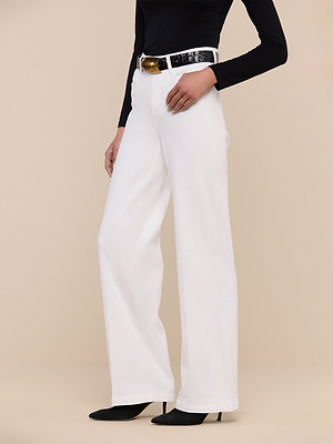 Wearing the Scottie Wide-Leg Jean, a black long-sleeve top, black textured belt, and black pointed-toe heels, a person stands against a beige background.