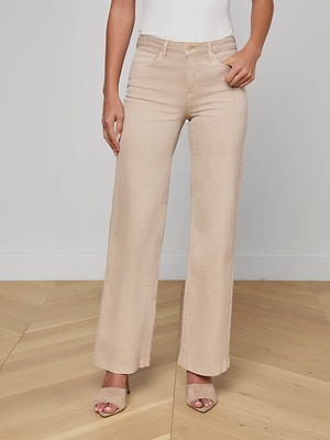 A person wearing Scottie Wide-Leg Jean beige pants and open-toed beige heeled sandals stands on a light wooden floor against a plain light wall, with their upper body partially out of frame.