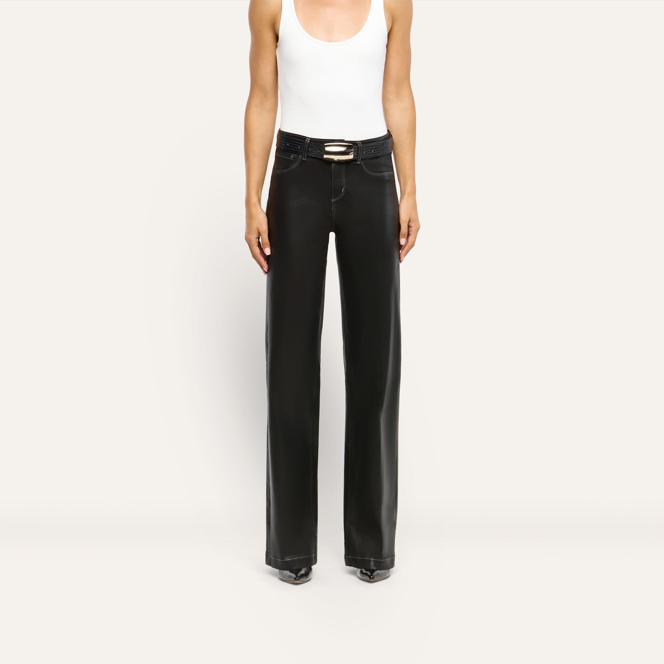 A person wearing a white tank top and Scottie Coated Wide-Leg Jean in black, styled as a high-rise, wide-leg fit with a belt.