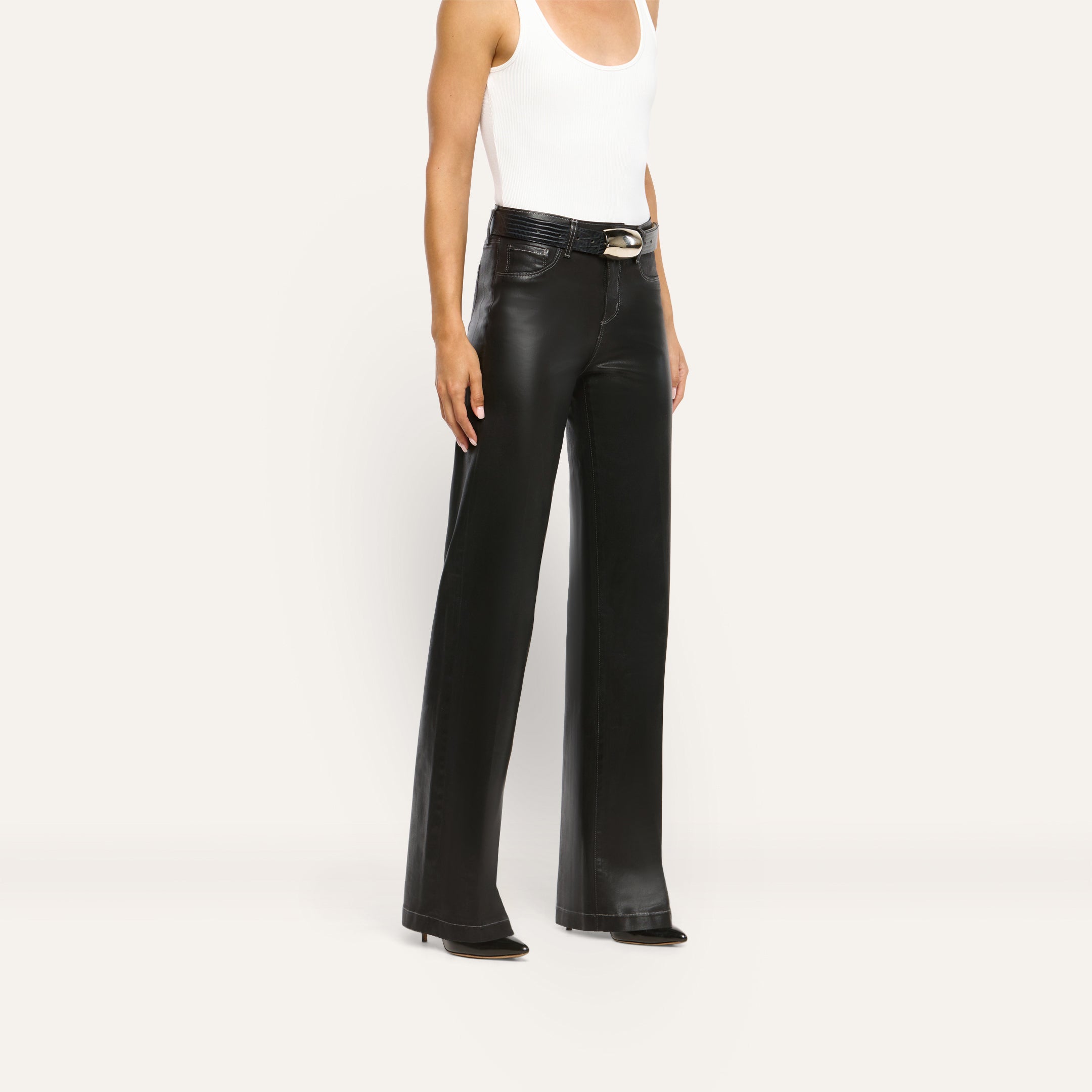 Person wearing a white tank top and black Scottie Coated Wide-Leg Jean trousers with a black belt and pointed-toe heels.