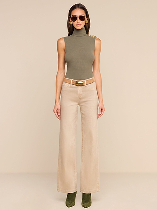 A woman wearing sunglasses, a sleeveless olive green turtleneck top, the Scottie Coated Wide-Leg Jean in beige with a belt, and green boots stands against a plain beige background.