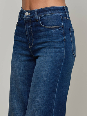 Close-up of a person wearing L'AGENCE Scottie Wide-Leg Jean in dark blue stretch denim, featuring a contoured waistband and front button, shown waist to mid-thigh against a neutral background.