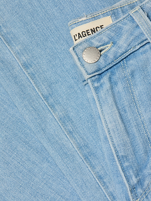 Close-up of Scottie Wide-Leg Jean in light blue stretch denim, featuring a front pocket, silver button, and partially visible white label with “L’AGENCE” in black.