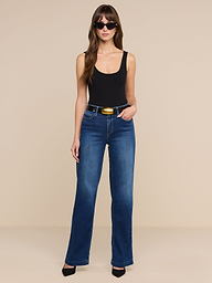 A woman stands against a plain white background, posing with one hand in her pocket, wearing a black tank top, the Scottie Wide-Leg Jean featuring stretch denim and a contoured waistband, paired with black heels and sunglasses.
