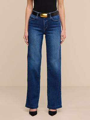 A person wears the Scottie Wide-Leg Jean with a contoured waistband, paired with a black top, black pointed-toe heels, and a black belt featuring a large gold buckle, standing against a plain beige background.