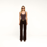 A woman wearing sunglasses, a brown sleeveless top, the Scottie Velvet Wide-Leg Jean—a pair of dark brown high-rise velvet pants with a contoured waistband—a belt, and brown boots stands against a plain white background.