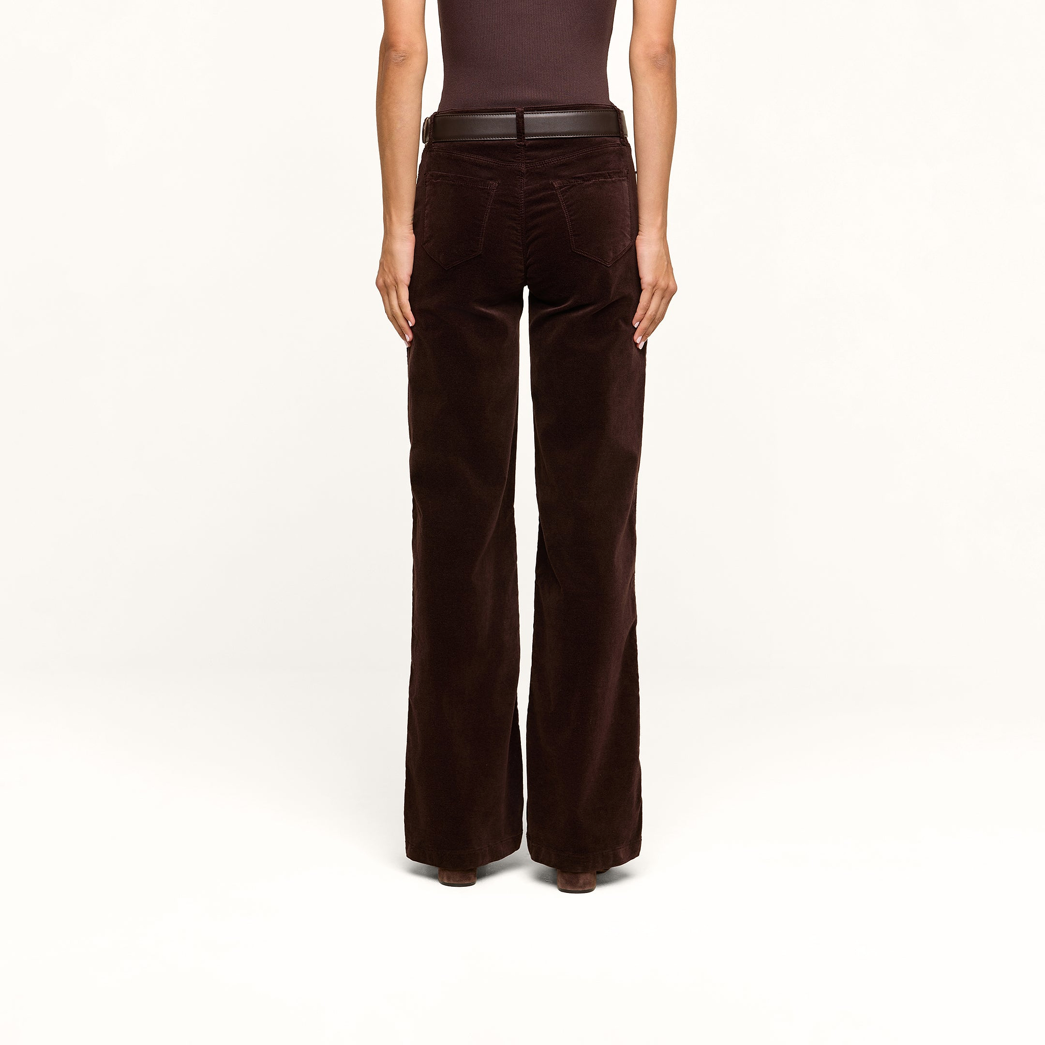 A person stands facing away, wearing a sleeveless brown top paired with the Scottie Velvet Wide-Leg Jean, featuring a contoured waistband and a black belt, set against a plain white background.