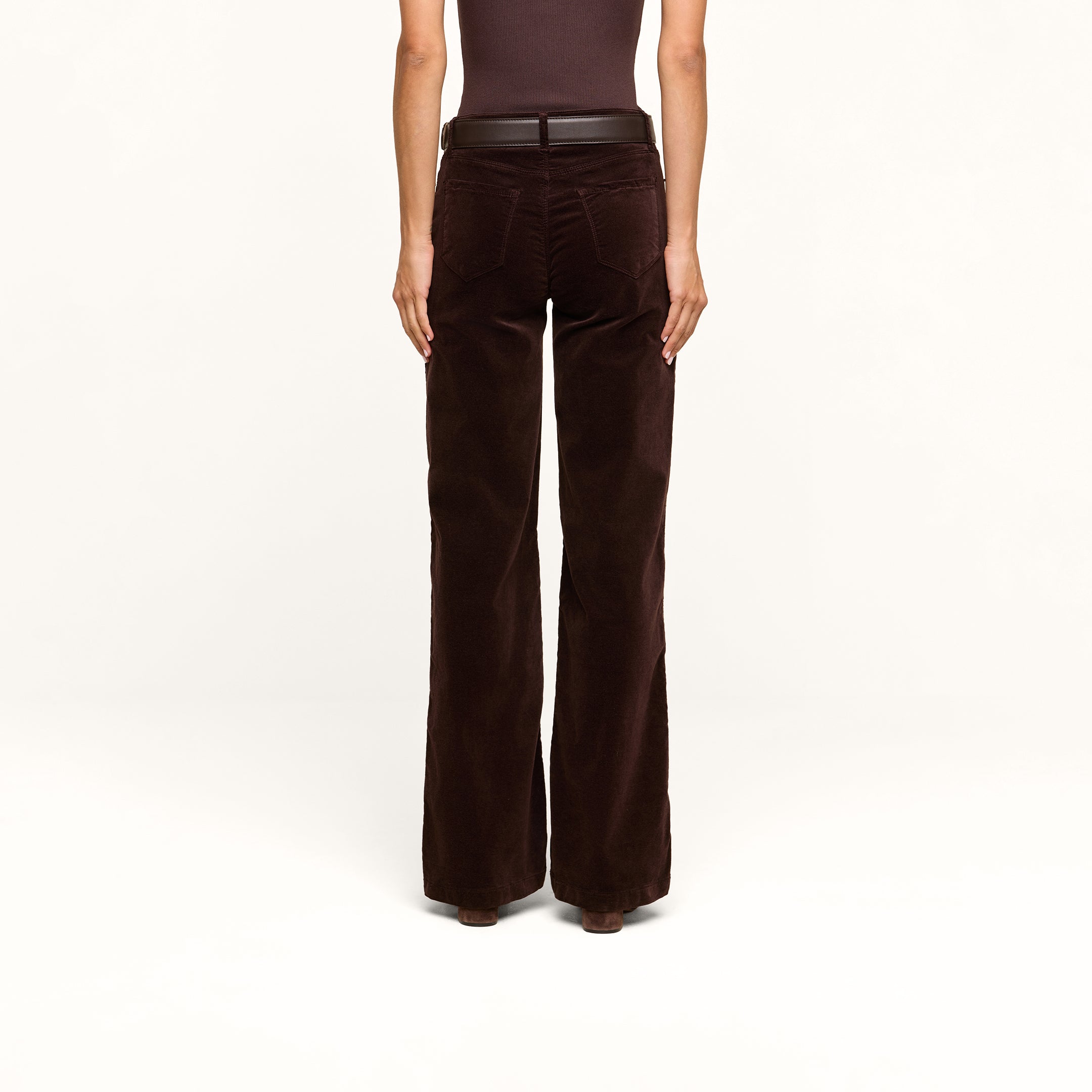 A person stands facing away, wearing a sleeveless brown top paired with the Scottie Velvet Wide-Leg Jean, featuring a contoured waistband and a black belt, set against a plain white background.