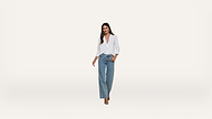 A woman wearing a white blouse and wide-leg blue jeans stands against a plain white background, looking confidently at the camera.