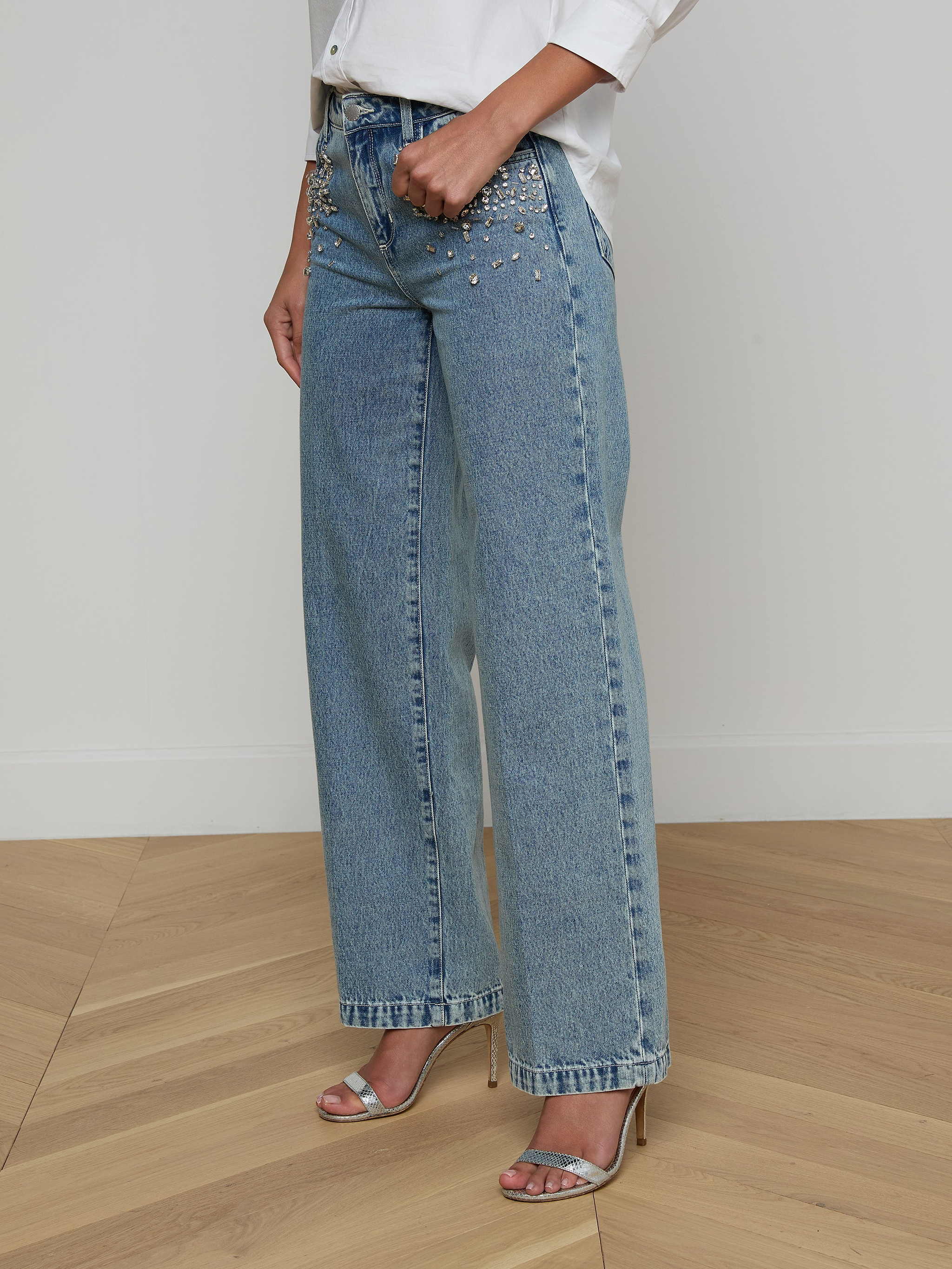 Model wearing the Scottie Embellished Wide-Leg Jean in light blue all-cotton denim with pearl detailing, paired with a white shirt and silver high-heeled sandals, shown from shoulders down against a plain background.