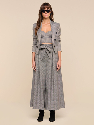 Woman wearing sunglasses, a gray plaid suiting blazer, a matching cropped top, the Lowen Pant—a wide-leg high-rise style with a paper-bag waist and tie belt—and black boots, standing against a plain beige background.