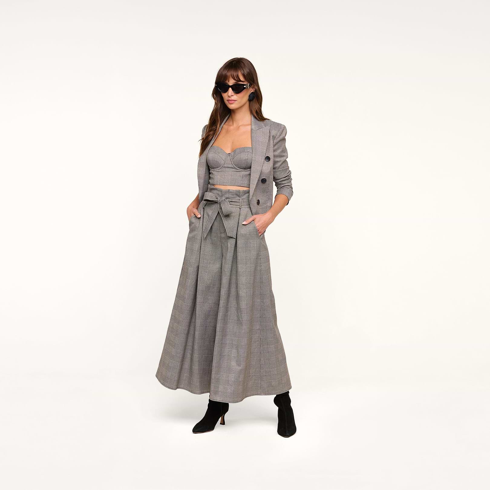 Woman wearing sunglasses, a gray plaid suiting blazer, cropped bustier top, and the Lowen Pant—high-rise, wide-leg pants featuring a paper-bag waist with a bow belt—paired with black ankle boots, standing against a plain white background.