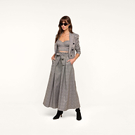 Woman wearing sunglasses, a gray plaid suiting blazer, cropped bustier top, and the Lowen Pant—high-rise, wide-leg pants featuring a paper-bag waist with a bow belt—paired with black ankle boots, standing against a plain white background.