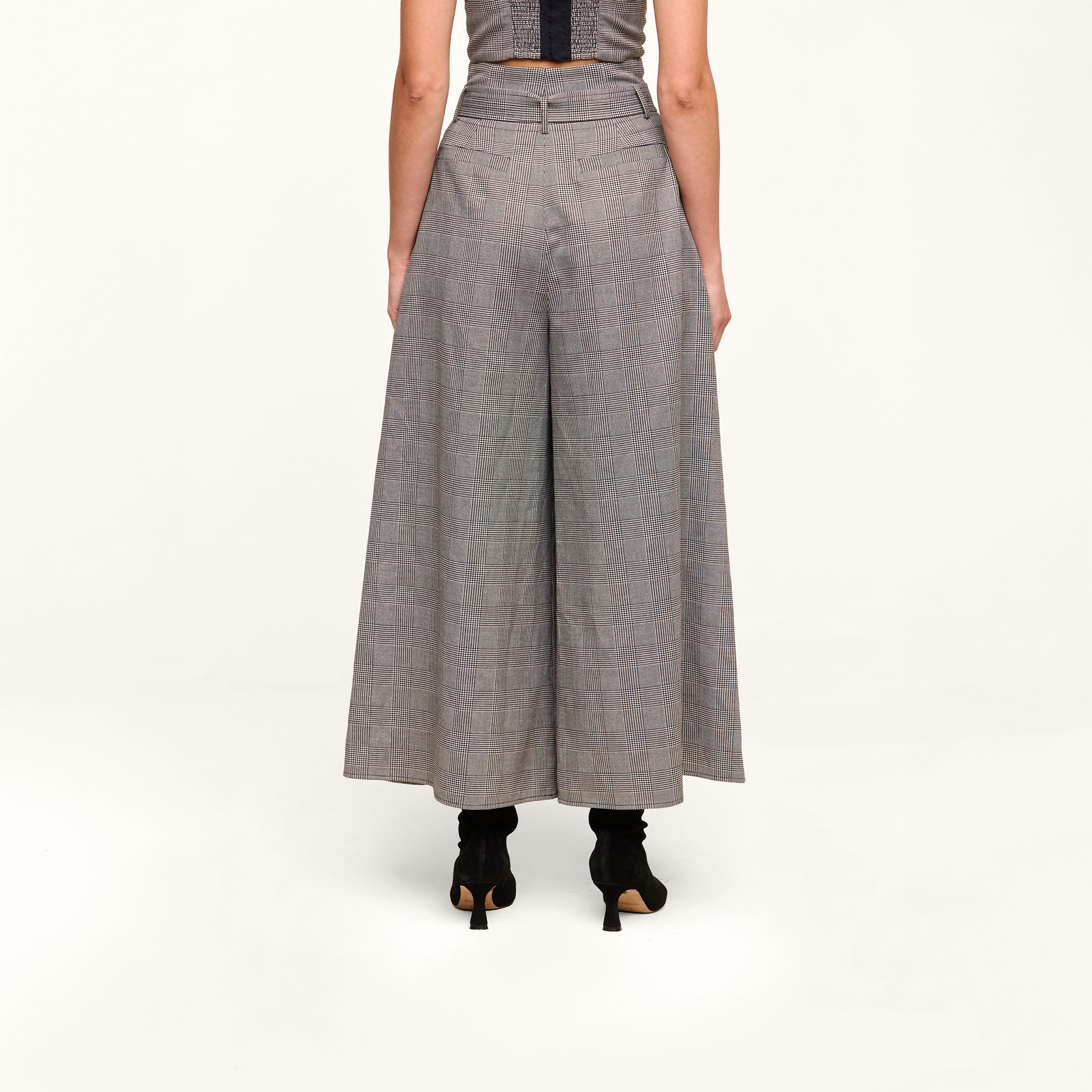 A person shown from the back, standing against a plain white background, is wearing the Lowen Pant—a high-rise plaid suiting wide-leg gray pant with a paper-bag waist—paired with black heeled shoes.