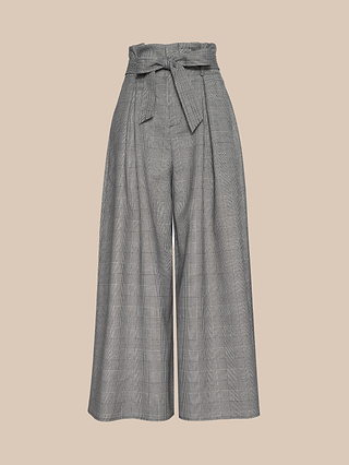 The Lowen Pant features a subtle plaid suiting pattern in gray, designed with a high-waisted, wide-leg culotte silhouette and a matching fabric belt tied at the paper-bag waist, showcased against a neutral beige background.