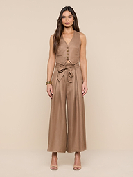 A woman stands facing forward, wearing the Lowen Linen-Blend Pant in tan, styled with a matching sleeveless top and a tied belt. She has long hair, neutral heels, and a bracelet, posing against a plain white background.