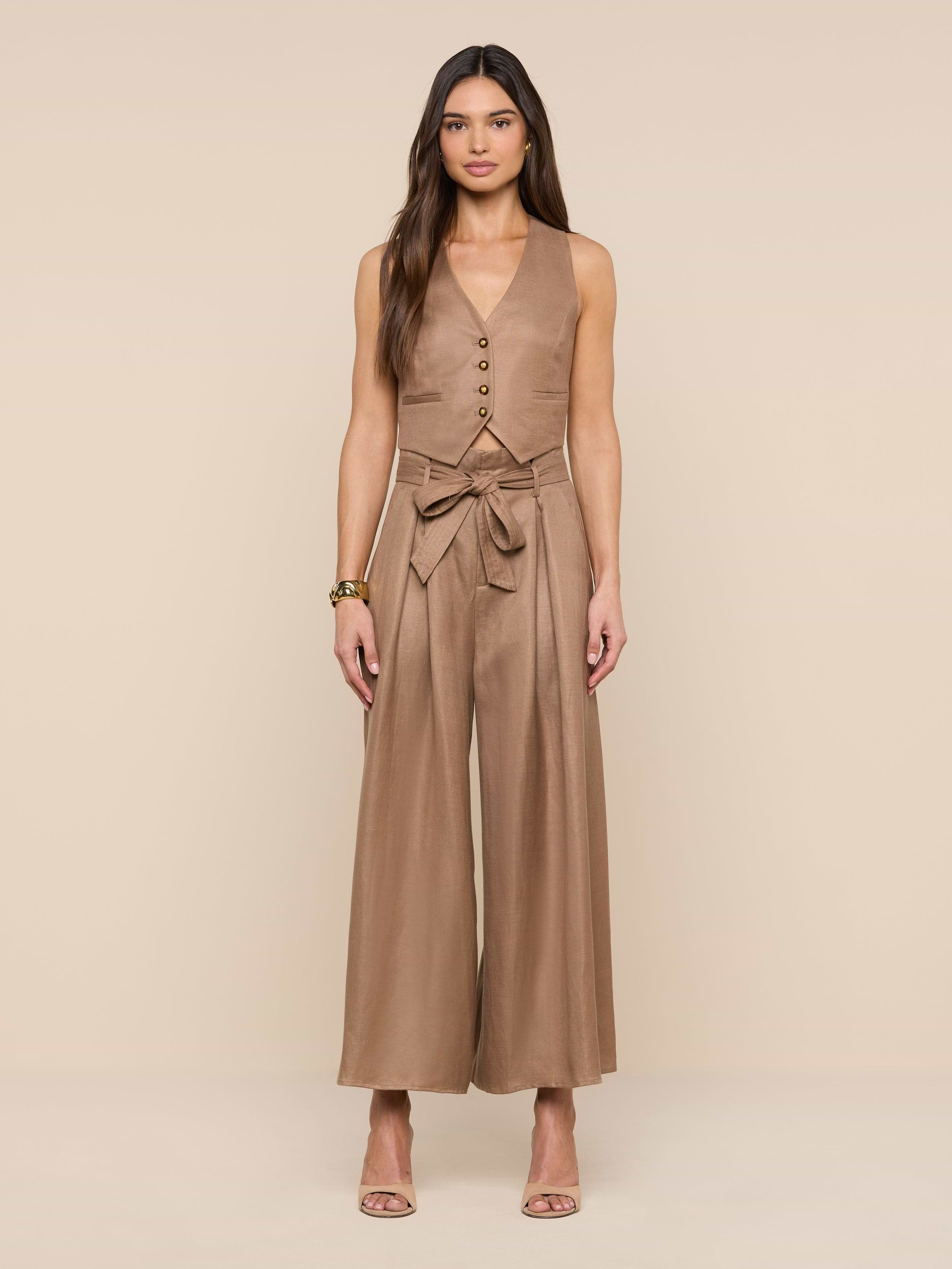 A woman stands facing forward, wearing the Lowen Linen-Blend Pant in tan, styled with a matching sleeveless top and a tied belt. She has long hair, neutral heels, and a bracelet, posing against a plain white background.