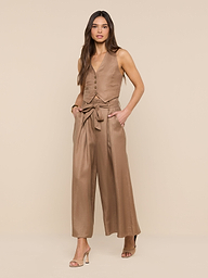 A woman stands against a white background, hands in her pockets, wearing tan open-toe heels and the Lowen Linen-Blend Pant—a wide-leg, cropped style with a tied belt—paired with a coordinating tan sleeveless buttoned vest.