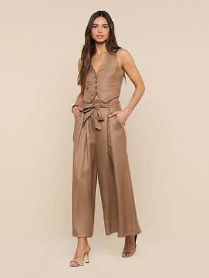 A woman with long hair stands against a beige background wearing the Lowen Linen-Blend Pant—high-rise, wide leg, with a waist tie—paired with a matching sleeveless vest and nude high-heeled sandals, hands in her pockets.