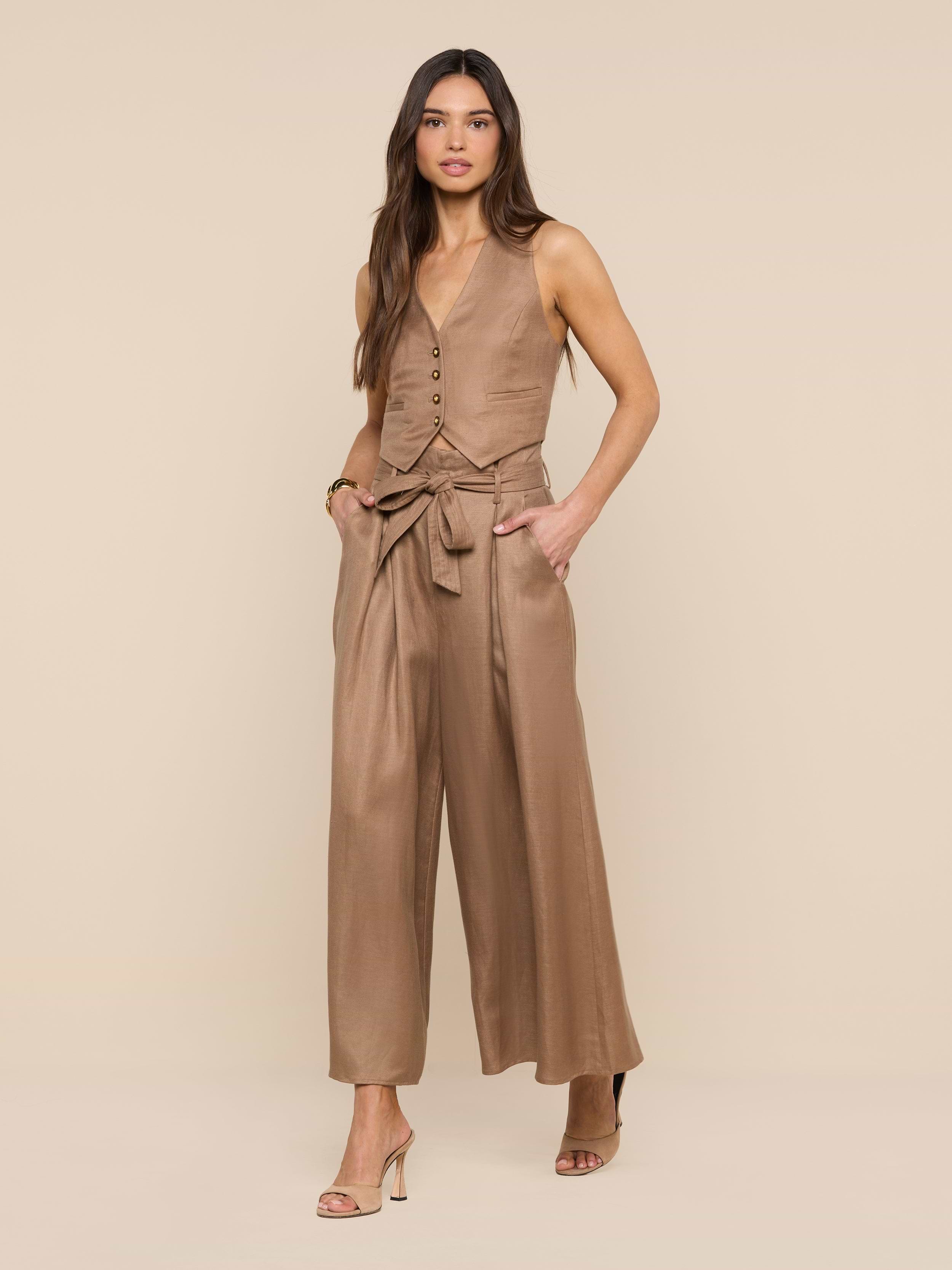 A woman stands against a white background, hands in her pockets, wearing tan open-toe heels and the Lowen Linen-Blend Pant—a wide-leg, cropped style with a tied belt—paired with a coordinating tan sleeveless buttoned vest.
