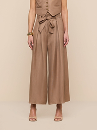 A person wearing a sleeveless tan vest, the Lowen Linen-Blend Pant featuring a wide cropped leg and tied waist, and tan heeled sandals stands against a plain white background.