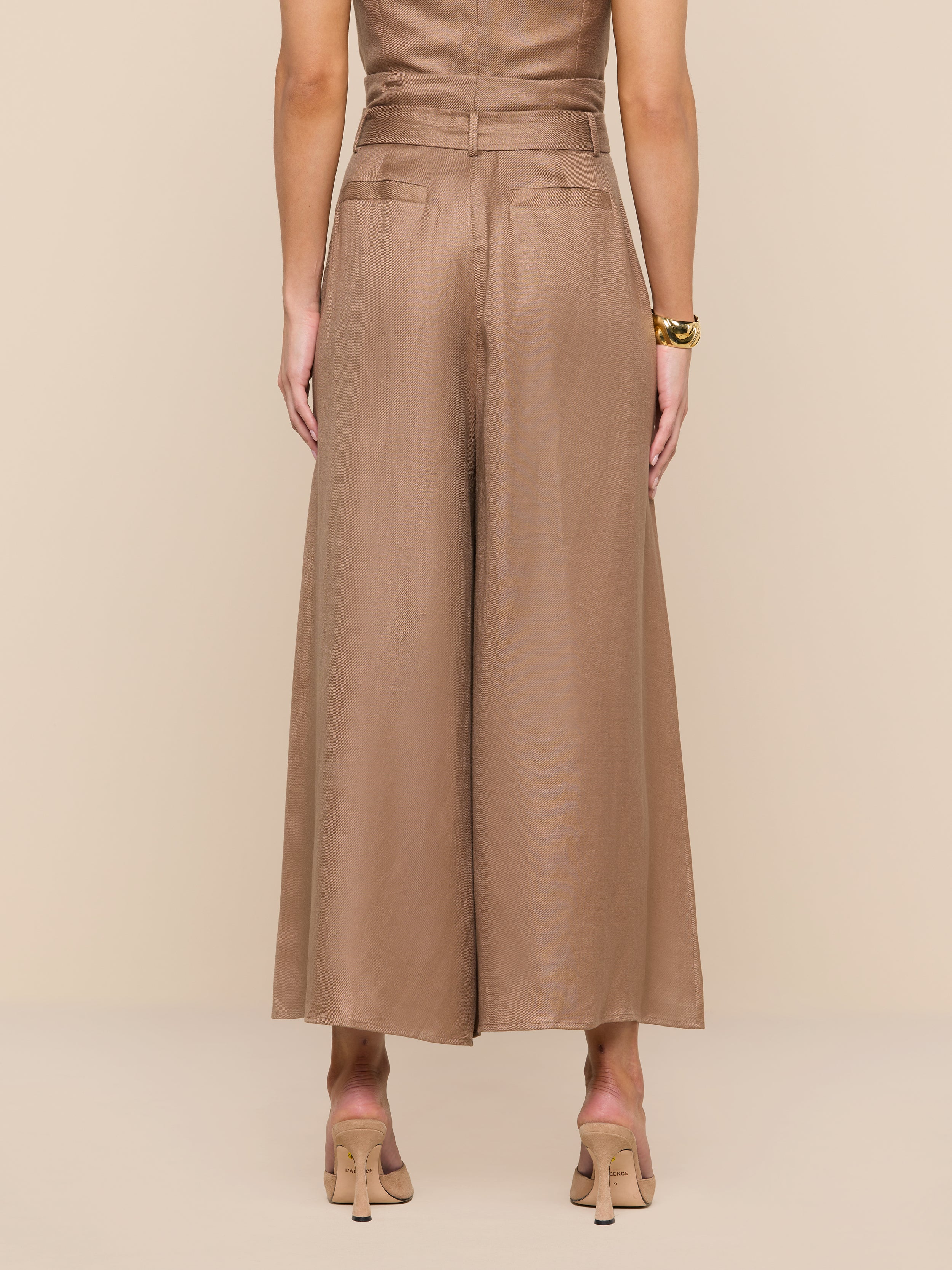 A person stands facing away, wearing the Lowen Linen-Blend Pant, featuring a wide cropped leg, paired with nude heels against a plain white background.