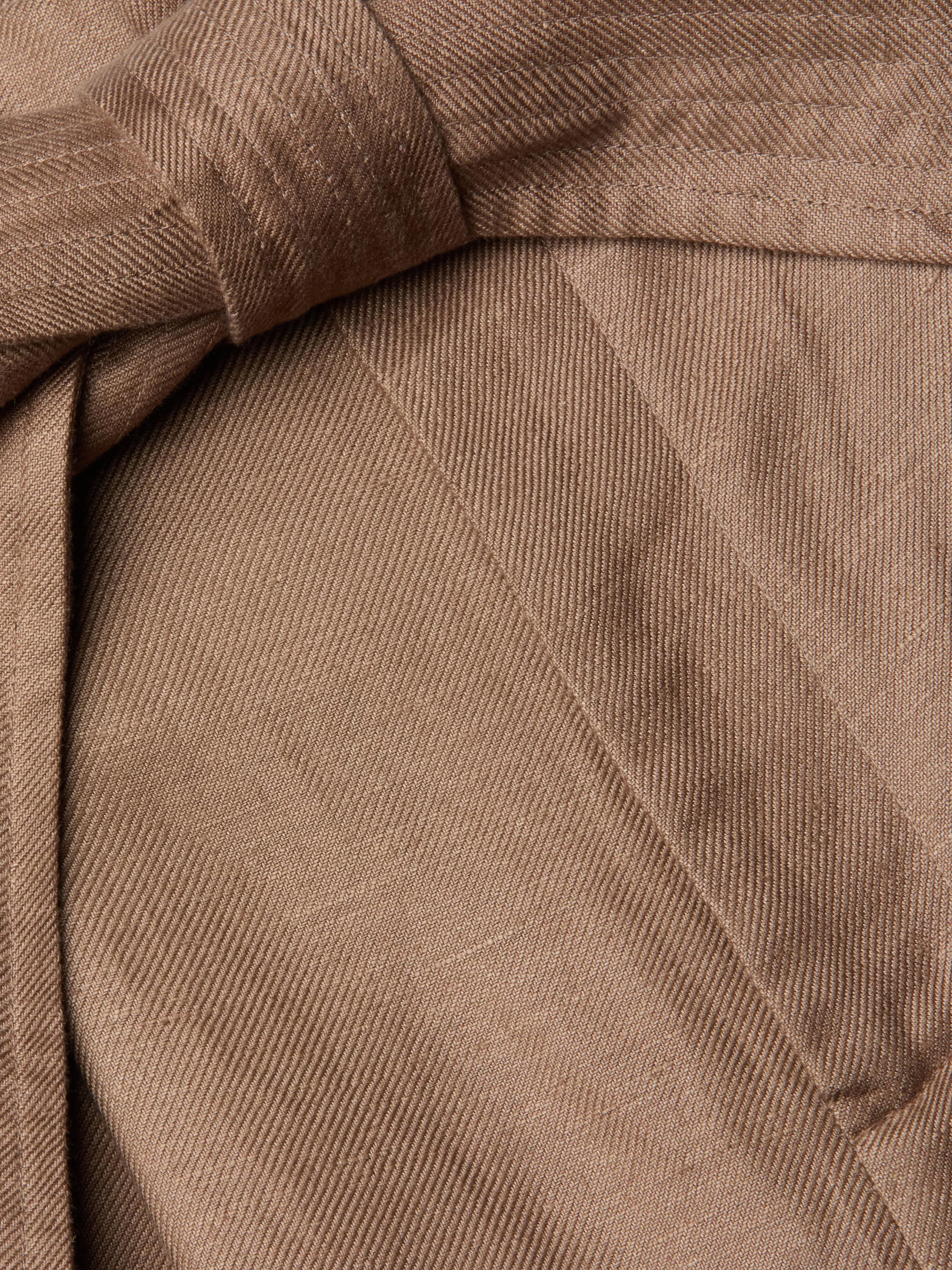 Close-up of brown linen-blend fabric with a visible twill weave pattern, highlighting a neatly sewn seam and a fabric fold or belt crossing over itself—details that reflect the refined tailoring of the Lowen Linen-Blend Pant with its wide cropped leg.