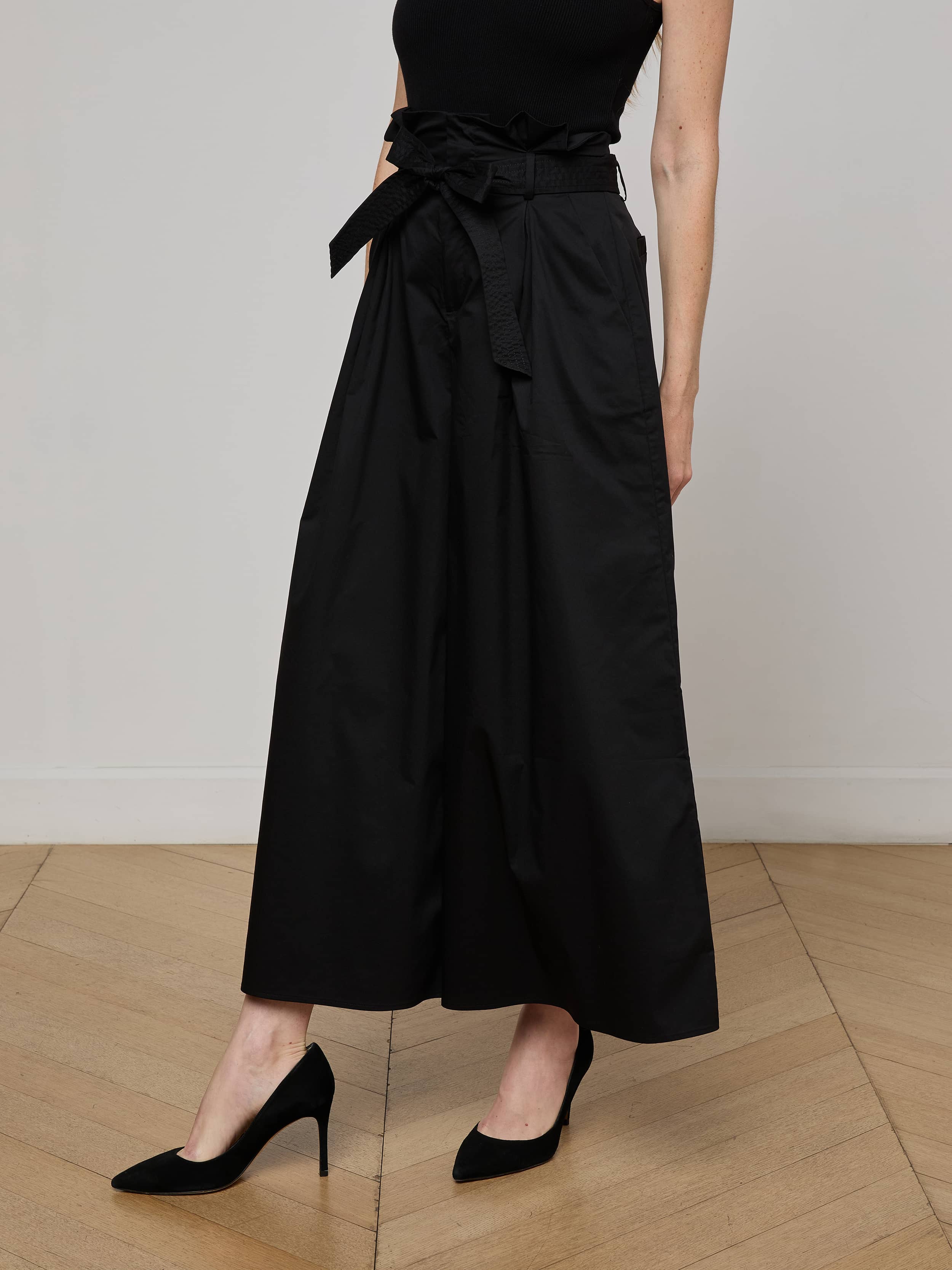 A person wears the Lowen Pant in black, styled with a sleeveless top and black high-heeled shoes. The lower half of the body is visible against a plain light background.