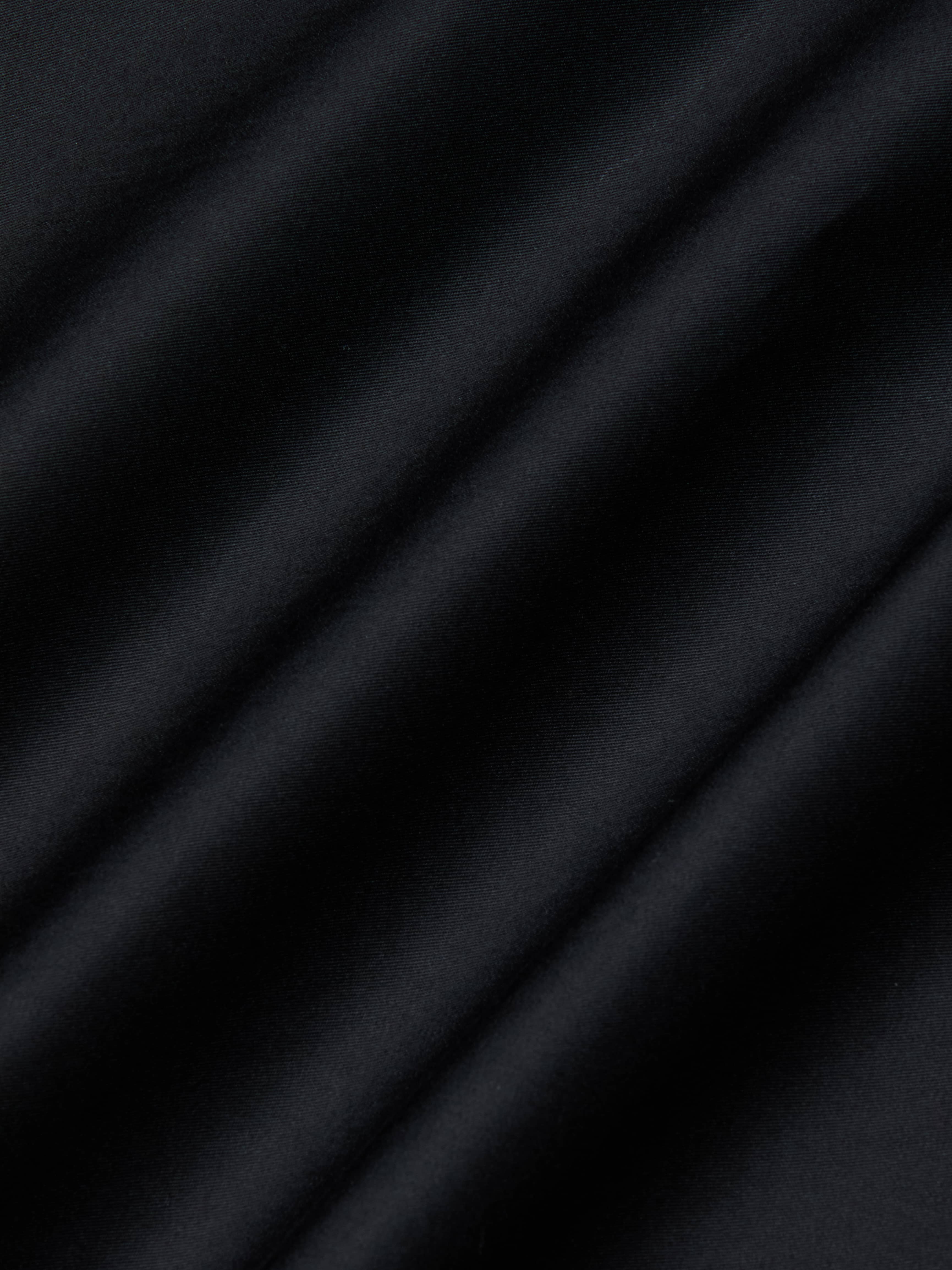 Close-up of the Lowen Pant’s black poplin fabric, featuring diagonal, soft shadows and a subtle texture that creates a striped pattern across the surface.