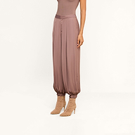 A person wearing the Palmer Satin Pant in a loose, mauve-colored satin style with gathered ankles and beige high-heeled boots, shown from the neck down against a plain background.