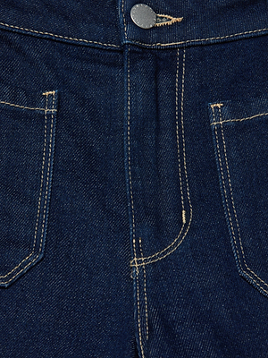 Close-up of the front of the Nolan Patch Pocket Jean in dark blue wash denim, featuring two front pockets, a metal button, zipper fly, and contrast stitching.