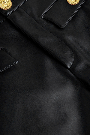 Close-up of L'AGENCE Dionne Vegan Leather Short in black, featuring two pockets and shiny gold buttons. Shows smooth vegan leather texture and detailed stitching—ideal for versatile styling.