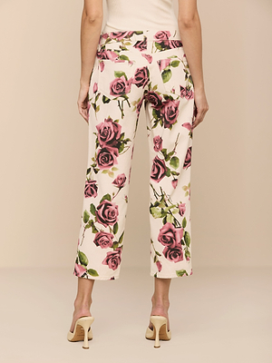 A person seen from the back wears Blaine Cropped Stovepipe Jeans featuring a pink and white floral print, paired with a white top and cream heels. The background is beige.