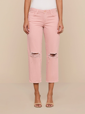 Wearing the Blaine Cropped Stovepipe Jean in light pink cotton denim, featuring high waist and frayed knee rips, paired with nude open-toed heels, a person stands against a beige background.