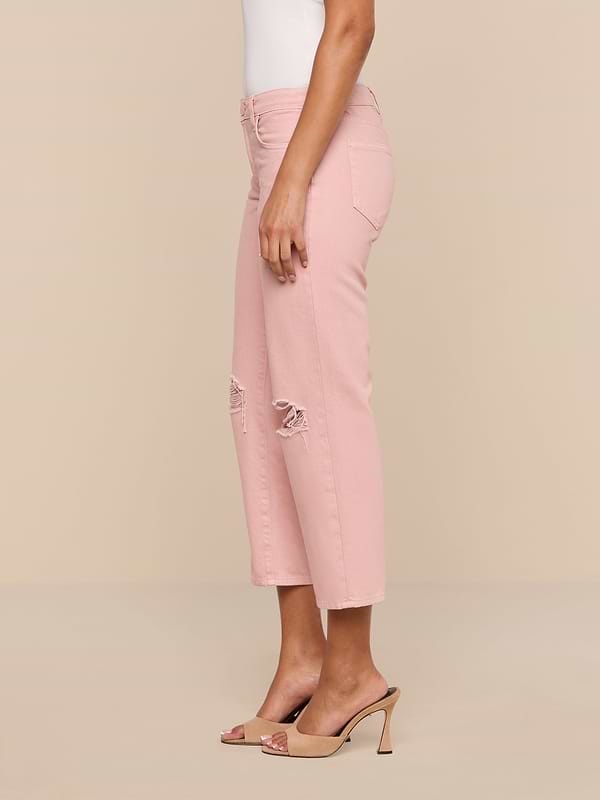 A person wearing the Blaine Cropped Stovepipe Jean in light pink with ripped knees, paired with a white sleeveless top and beige high-heeled sandals, stands sideways against a plain white background.