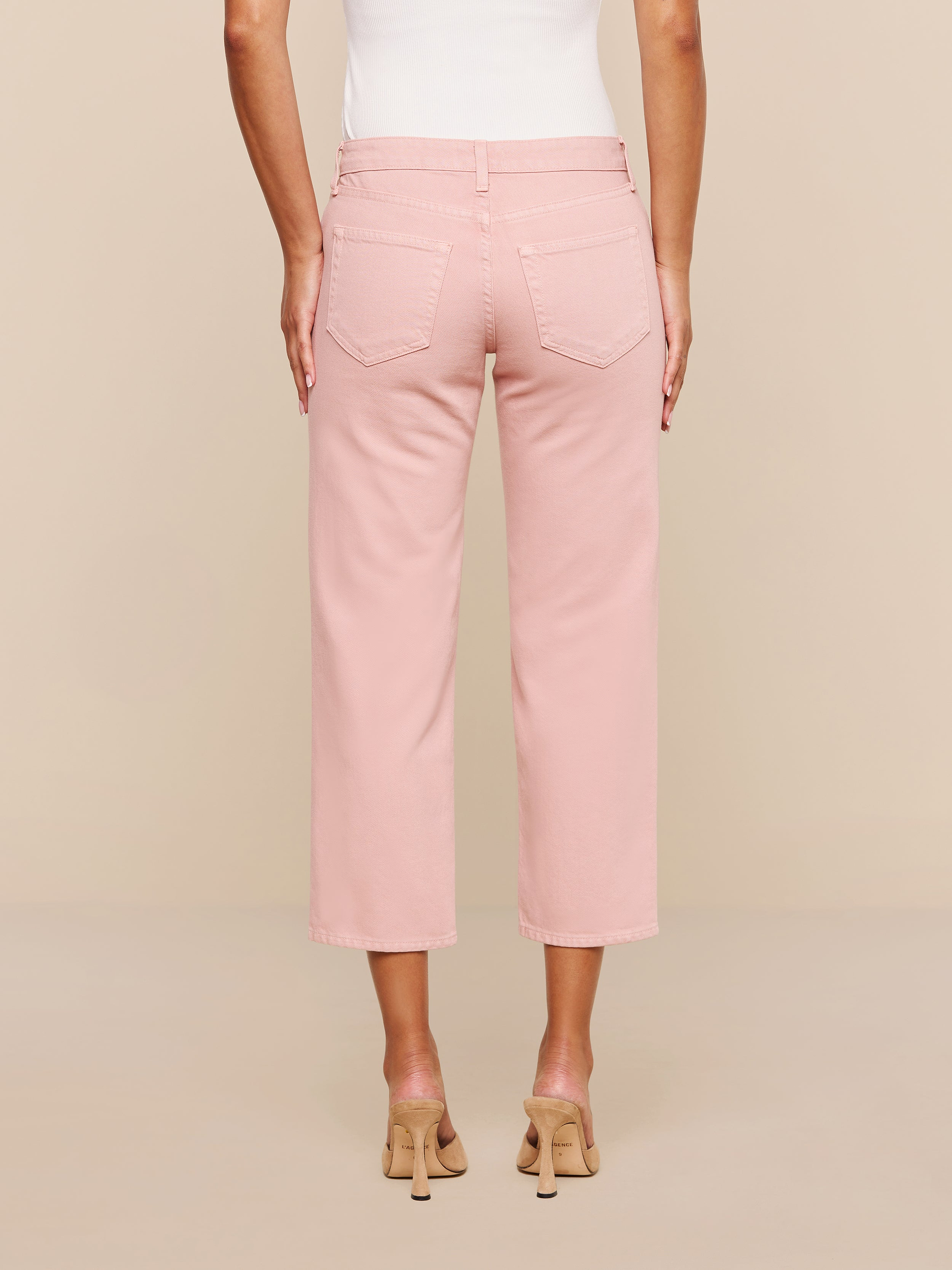 A person is shown from the back against a plain white background wearing the Blaine Cropped Stovepipe Jean in light pink, paired with a white sleeveless top and beige heeled sandals.