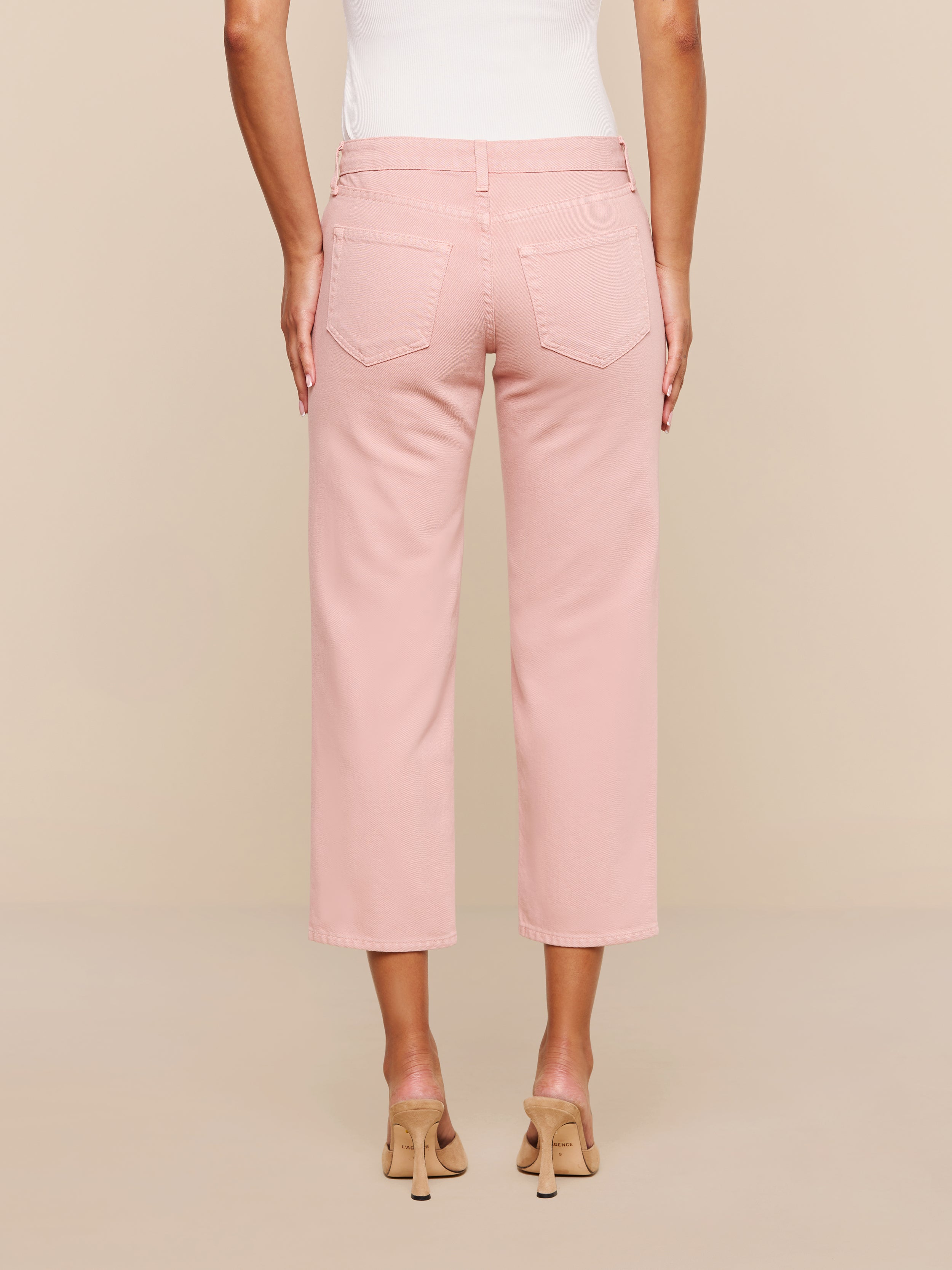 A person is shown from the back against a plain white background wearing the Blaine Cropped Stovepipe Jean in light pink, paired with a white sleeveless top and beige heeled sandals.