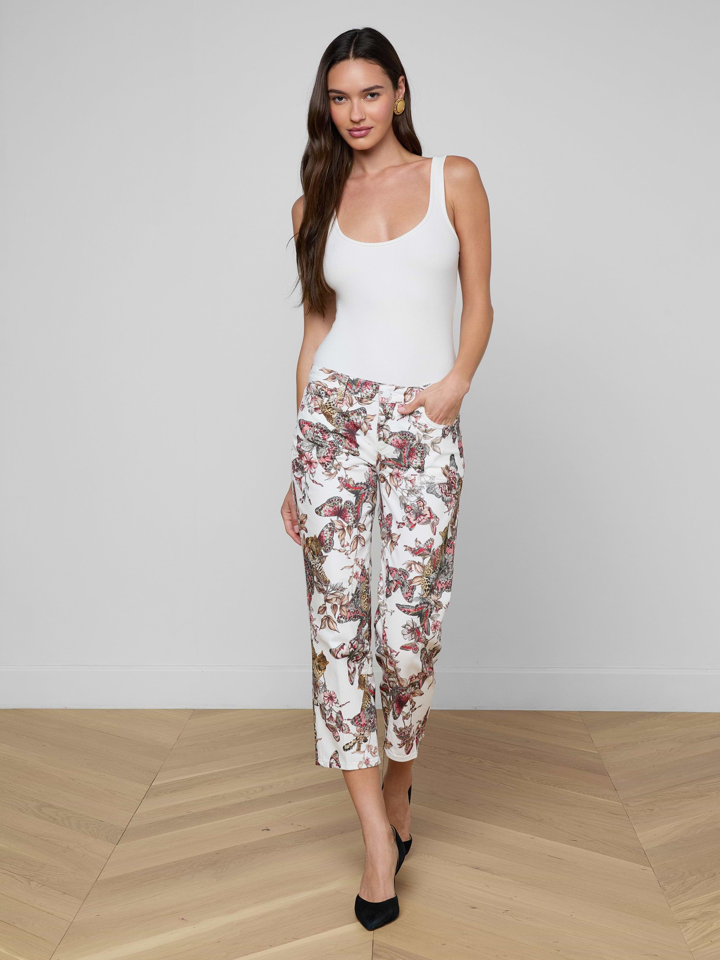 A woman stands against a plain, light background with one hand in her pocket, wearing a white tank top and the Blaine Cropped Stovepipe Jean.