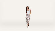 A woman in a white tank top and floral wide-leg pants stands against a plain white background, with one hand in her pocket and wearing black heels.