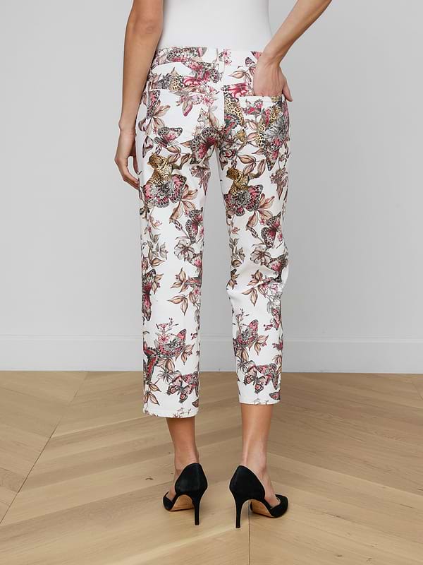 A person is seen from the back wearing the Blaine Cropped Stovepipe Jean in white with a floral print, styled with black high heels and one hand in a pocket, against a plain light background.