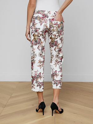 A person stands on a wooden floor wearing the Blaine Cropped Stovepipe Jean in white with a colorful floral pattern, paired with black high heels. The back view shows one hand tucked casually in a pocket.