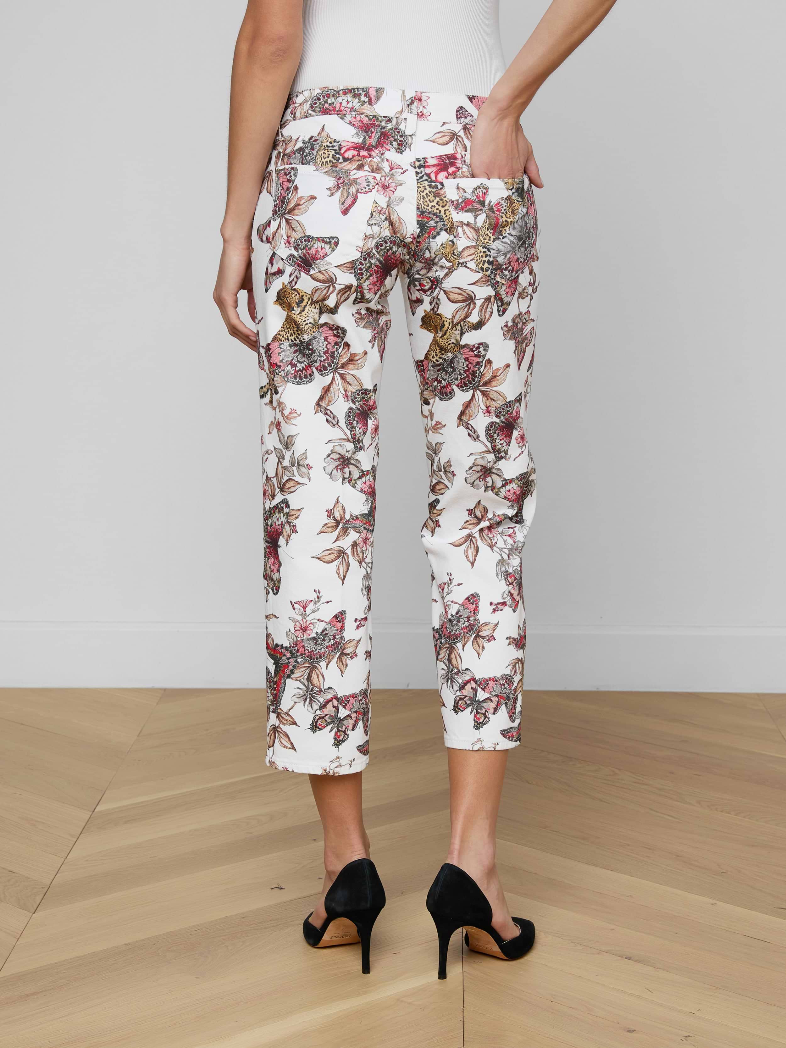 A person is seen from the back wearing the Blaine Cropped Stovepipe Jean in white with a floral print, styled with black high heels and one hand in a pocket, against a plain light background.
