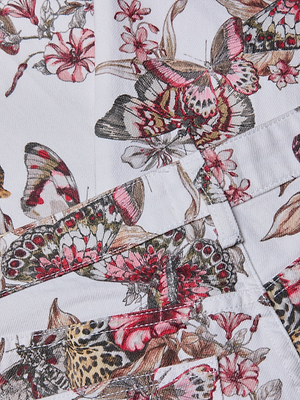 Close-up of the Blaine Cropped Stovepipe Jean’s white fabric, featuring a detailed butterfly and pink flower print at the seams in shades of pink, red, black, and beige—perfect for lovers of bold patterns.