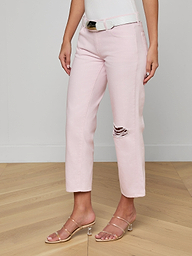 A woman wears the Blaine Cropped Stovepipe Jean in pale pink, styled with a white belt, white tank top, and strappy nude heels. The jeans have a single ripped detail on one knee. The background is plain and off-white.