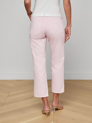 Someone stands with their back to the camera on a light wood floor, wearing a white top, clear-heeled sandals, and pastel lilac Blaine Cropped Stovepipe Jeans.