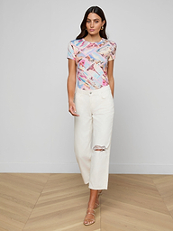 A woman wearing a colorful graphic t-shirt, Blaine Cropped Stovepipe Jeans made from all-cotton denim, and beige heeled sandals stands against a plain white background.