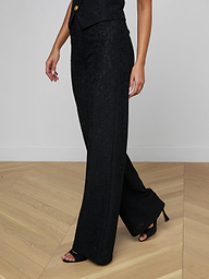 A person wearing the Livvy Lace Trouser—a pair of high-rise black wide-leg pants—and open-toed black heels is shown from the shoulders down, posing against a plain light background.