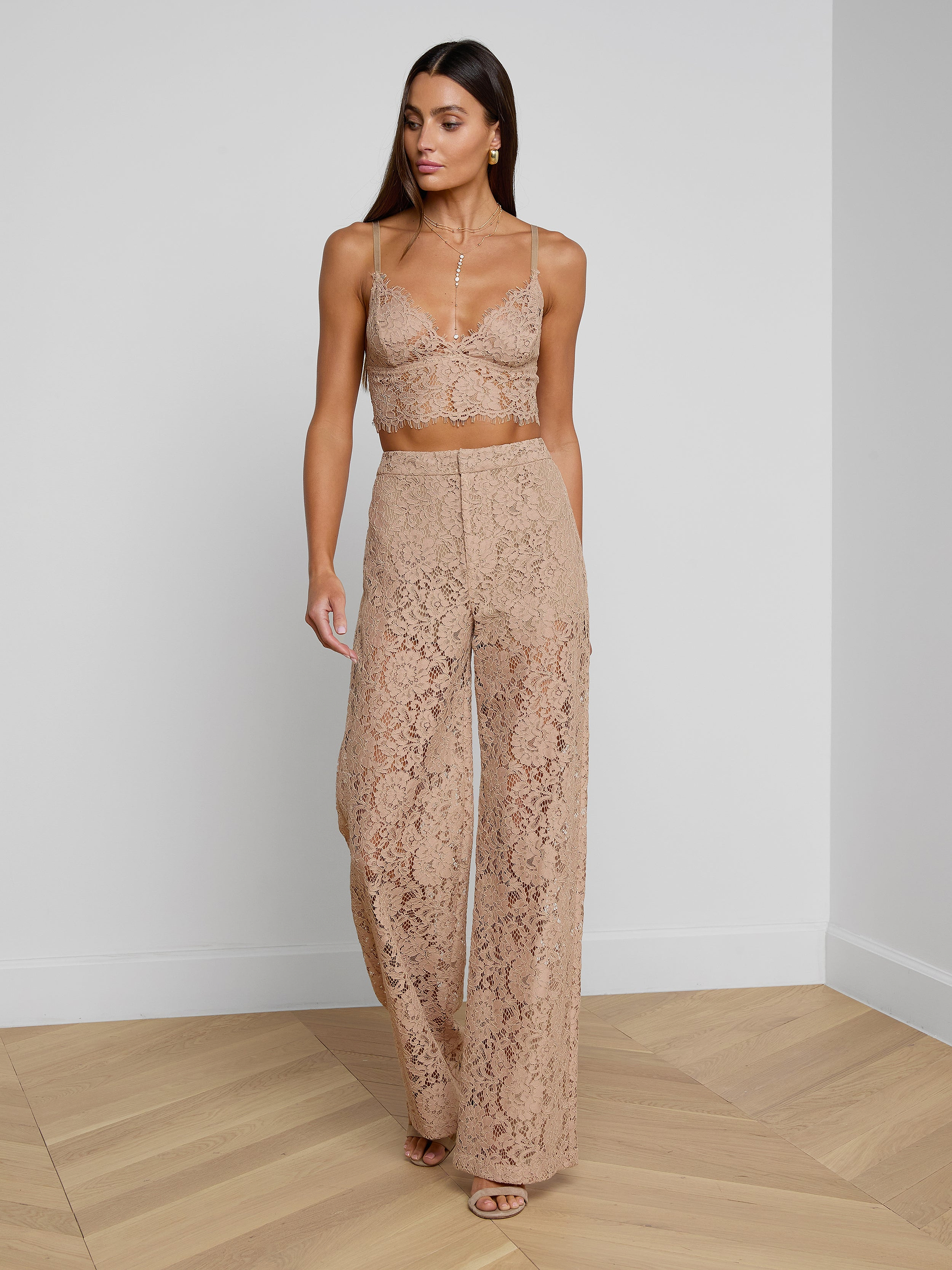 A woman wearing the Livvy Lace Trouser, styled with a matching nude floral lace crop top and nude heels, walks against a plain white background.